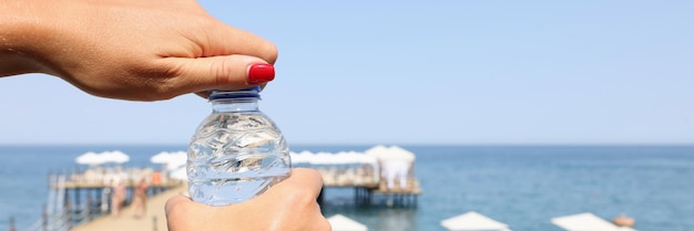 Vrouw handen open fles water buiten op het strand drinkregime tijdens hete seizoen concept