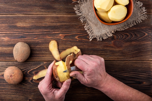 Vrouw handen schillen aardappel. maak aardappelen op een houten oppervlak schoon. voedsel repareren om te koken.