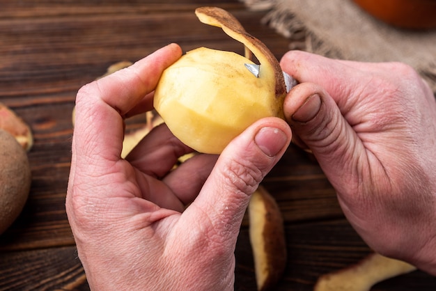 Vrouw handen schillen aardappel. maak aardappelen op een houten oppervlak schoon. voedsel repareren om te koken.