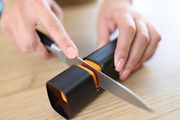 Foto vrouw handen slijpen mes met puntenslijper op keukentafel close-up