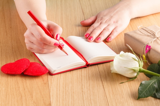 Vrouw handen tekenen of schrijven, geschenkdoos, rode harten op houten tafel