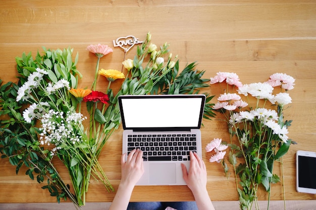 Vrouw handen typen op toetsenbord op een laptop met wit scherm omringd door kleurrijke verse bloemen en inscriptie liefde is Valentijnsdag concept