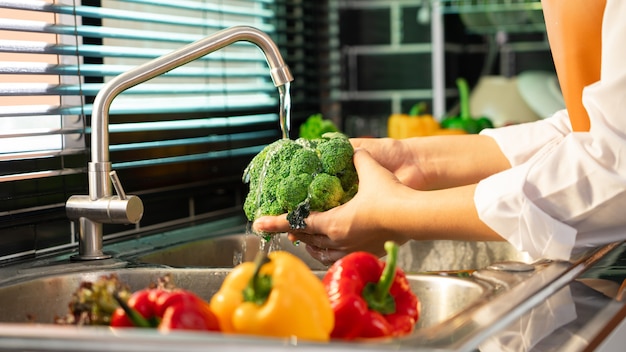 Vrouw handen wassen groenten voor de bereiding van veganistische salade