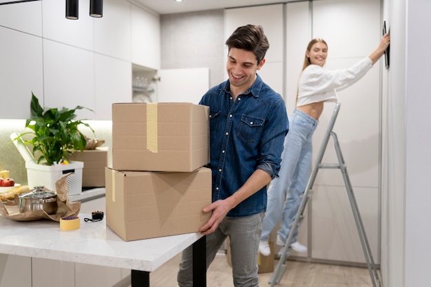 Vrouw hangt frame aan de muur terwijl haar vriend dozen hanteert