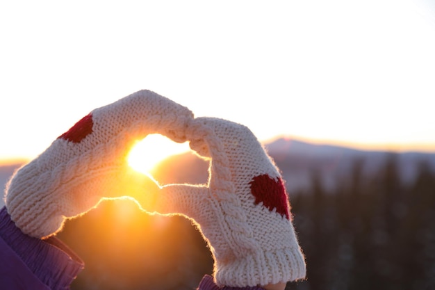 Vrouw hart maken met haar handen in de bergen bij zonsondergang close-up Wintervakantie