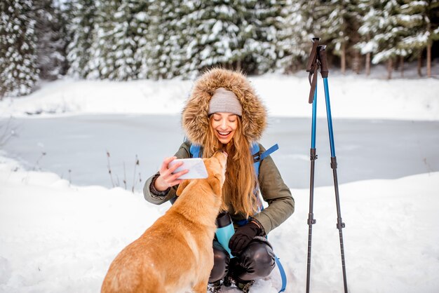 Vrouw heeft een pauze tijdens de winterwandeling en maakt selfie met haar hond in de besneeuwde bergen bij het meer en het bos
