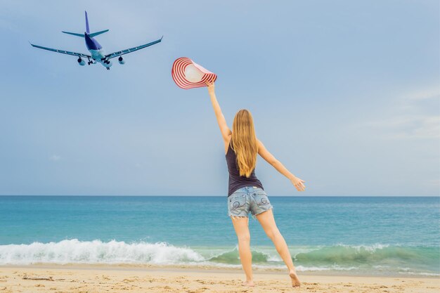 Vrouw heeft plezier op het strand en kijkt naar de landende vliegtuigen Reizen met een vliegtuigconcept