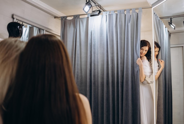 Vrouw helpt bruid trouwjurk te dragen in boetiek