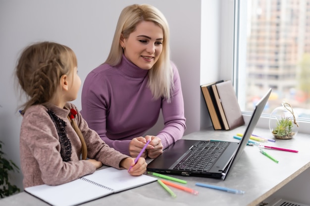 Vrouw helpt jong meisje met laptop huiswerk te maken in de eetkamer