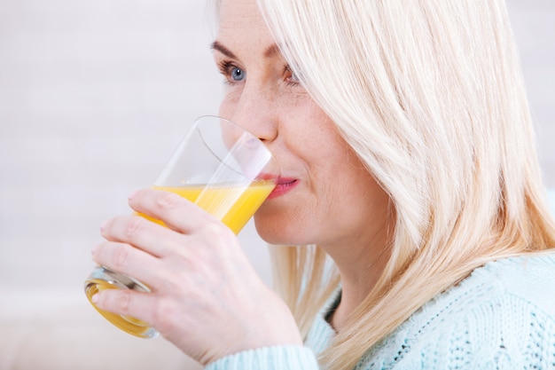 Foto vrouw het drinken jus d'orange het glimlachen. mooie middelbare leeftijd blanke model gezicht close-up.