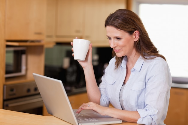 Vrouw het drinken thee terwijl op laptop