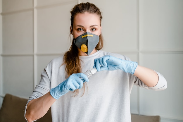 Vrouw het openen fles met handdesinfecterend middel die masker en handschoenen thuis dragen