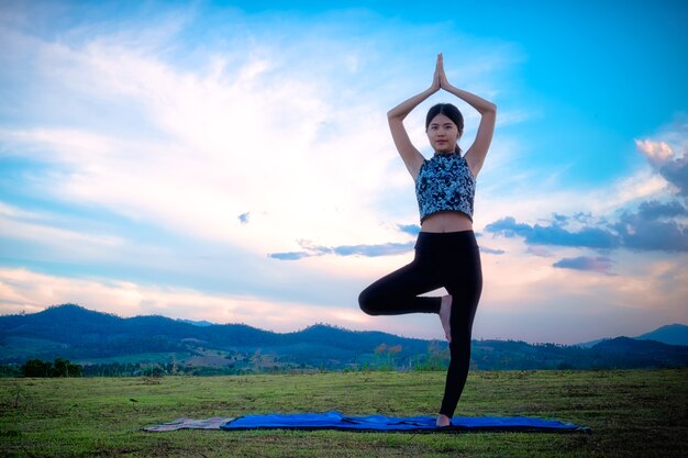 Vrouw het praktizeren yoga stelt in openlucht over de achtergrond van de zonsonderganghemel.