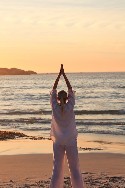 Vrouw het praktizeren yoga tijdens de zonsondergang bij het strand