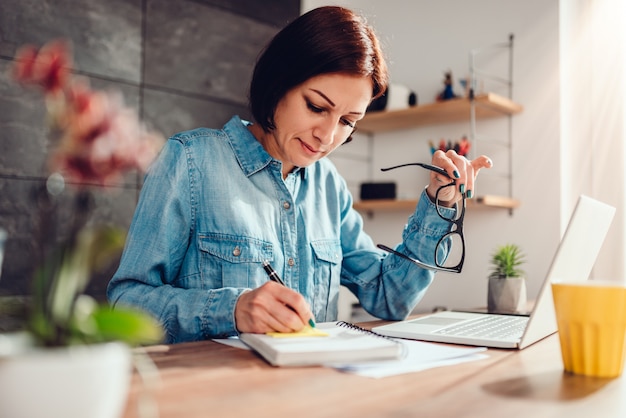 Vrouw het schrijven nota's in blocnote en holdingsglazen