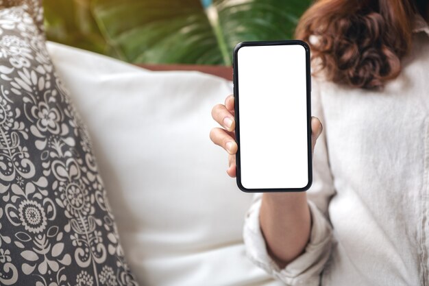 vrouw houden en zwarte mobiele telefoon met leeg wit scherm op de tafel in het moderne café tonen