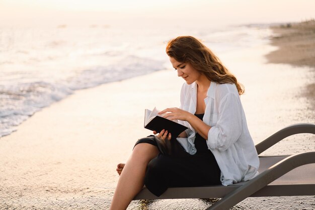 Vrouw houdt boek in haar handen en leest het boek op een zee tijdens zonsondergang