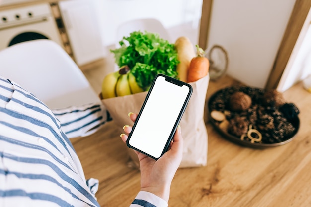 Vrouw houdt de smartphone met wit scherm vast, mock up. Online voedselmarktconcept.