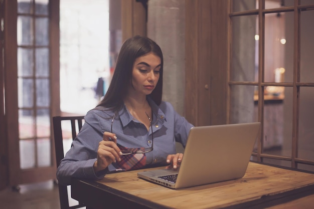 Vrouw houdt een bril in een hand en werkt met laptop