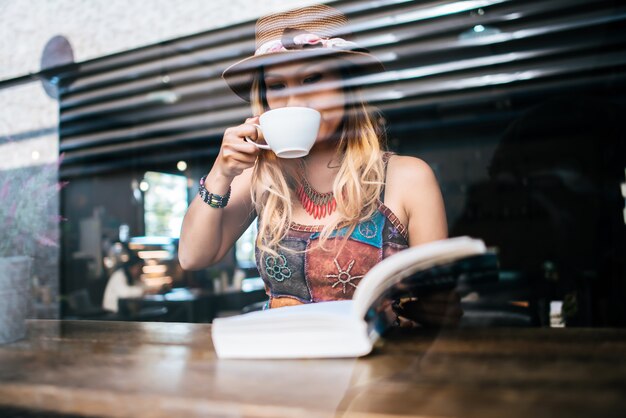 vrouw houdt een kop warme cappuccino en het lezen van een boek