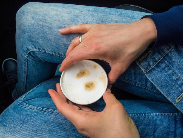 Vrouw houdt een kopje koffie in de auto Reislevensstijl Benen in spijkerbroek