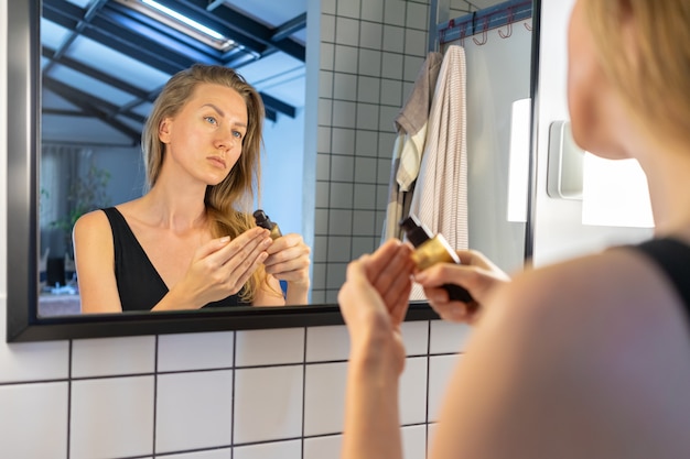 vrouw houdt een potje crème gezichtshuid moisturizer voor spiegel