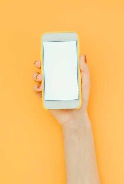 Vrouw houdt een smartphone met een wit scherm op het oranje oppervlak