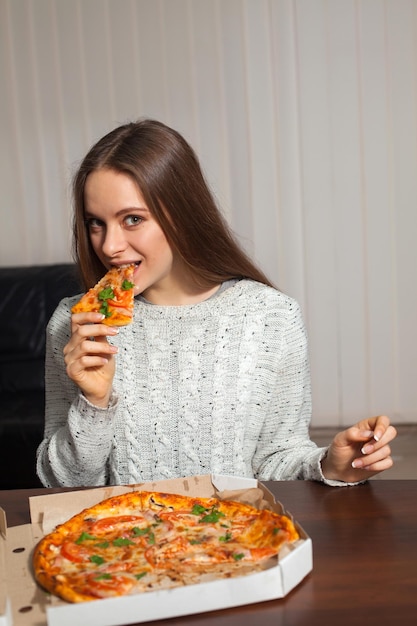 Vrouw houdt een stuk pizza in haar hand en wil het opeten