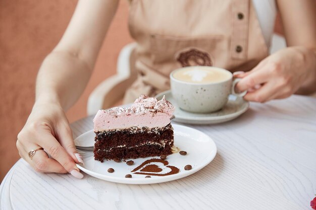 Vrouw houdt fruitchocoladetaart en kopje cappuccino op houten tafel buiten op het terras van het café Sfeervolle koffietijd voor jezelf Hartvormige dessertdecoraties