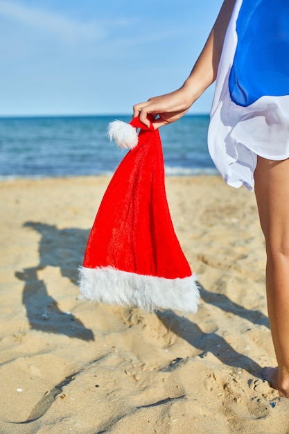 Vrouw houdt in de hand kerst kerstmuts staande op het strand