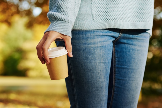 Vrouw houdt kopje koffie afhaalmaaltijden in herfst park