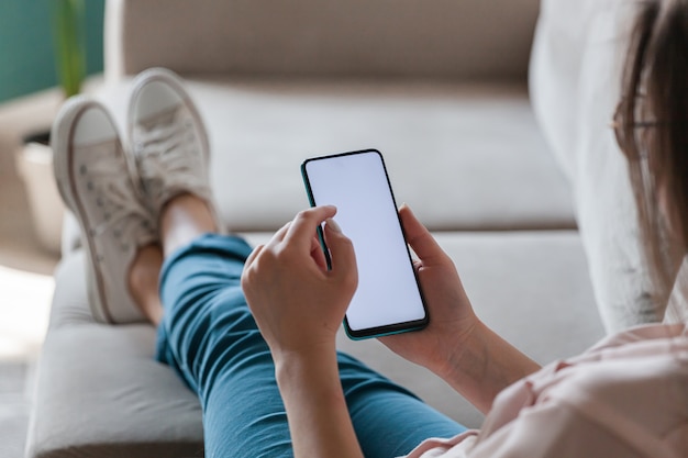 Vrouw houdt mobiele telefoon in handen, liggend op de bank