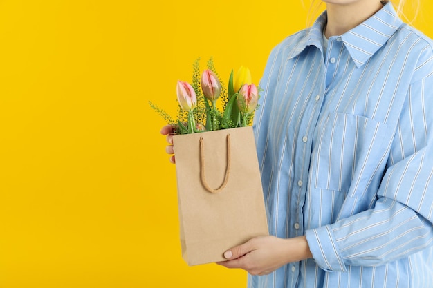 Vrouw houdt papieren zak met bloemen op gele achtergrond