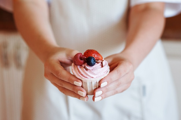 Vrouw houdt romige cupcake met verse bessen in haar handen voor het schort. Heerlijk huisgemaakt of restaurantdessert.