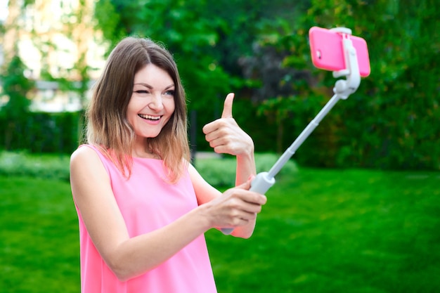 Vrouw houdt selfie stick met mobiel met gezichtsuitdrukking en stuur grappige selfie met grote vinger naar familieleden van vakantie