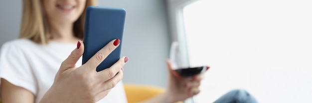 Vrouw houdt smartphone en glas rode wijn in haar handen