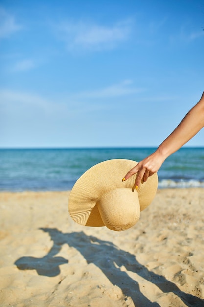 Vrouw houdt strohoed in de hand op het strand in de buurt van de zee