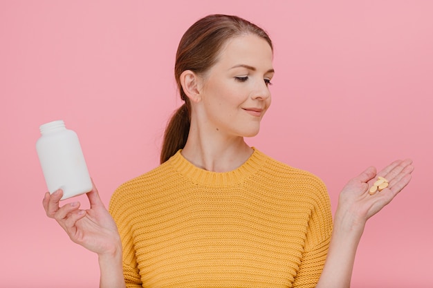 Vrouw houdt tube met vitamines in de hand en pillen op haar handpalm draagt gele trui