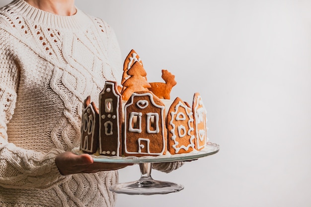 Vrouw houdt zelfgemaakte cake vast met gevels van peperkoekenhuis, een kerstboom en rendieren op een glazen standaard
