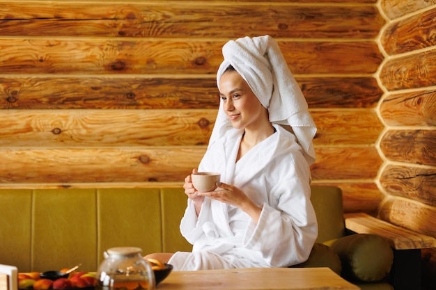 Vrouw in badjas en handdoek die thee drinkt na spabehandelingen