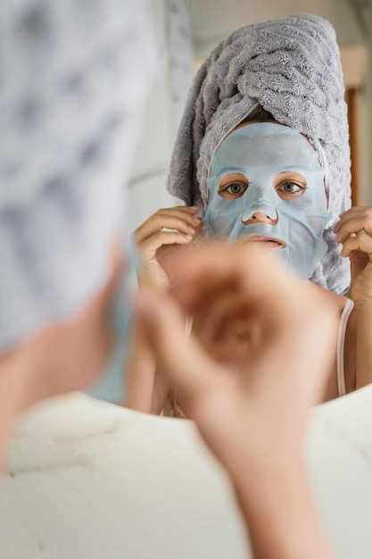 Vrouw in badkamer met aangebracht bladmasker op haar gezicht in de spiegel kijkend