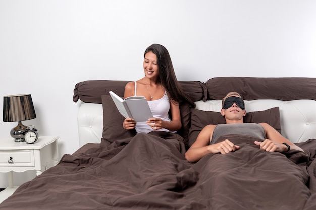 vrouw in bed en geniet van het lezen van een boek, terwijl haar jonge man slaapt