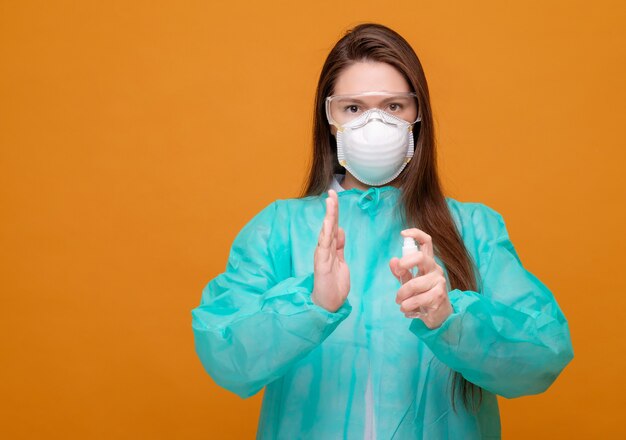 Vrouw in beschermende medische apparatuur met antisepticum in handen medisch masker op gezicht op gele coronavirus pandemie