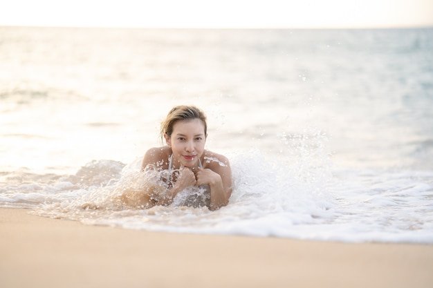 Vrouw in bikini die op zandstrand in het water ligt.