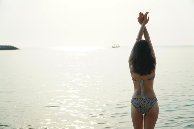 Vrouw in bikini die yoga doet en mediteert op het strand aan zee voor een ontspannende dag