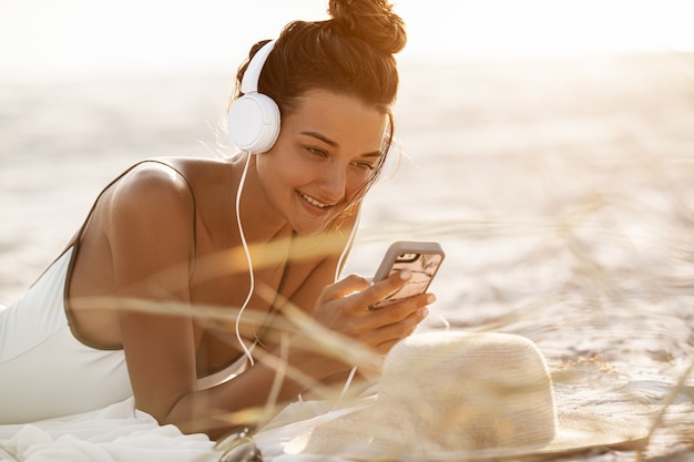 Vrouw in bikini met een smartphone en koptelefoon op het strand