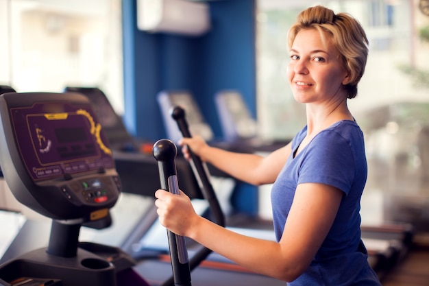 Vrouw in blauw shirt en kort haar opleiding in cardio-zone in de sportschool. Mensen, fitness en gezondheidsconcept