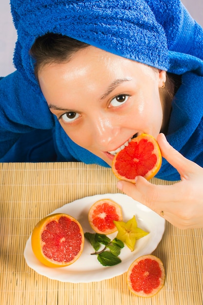 Vrouw in blauwe handdoek eet grapefruit en gebruikt voor huidbehandeling.