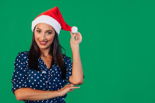 Vrouw in blauwe jurk en kerstmuts glimlachend op groene achtergrond