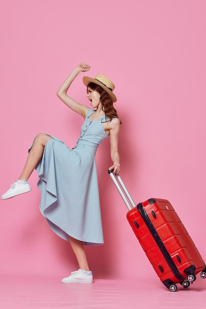 Vrouw in blauwe jurk met rode koffer reisbestemming roze achtergrond